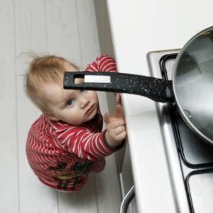 child safety at home concept - toddler reaching for pan on the stove in kitchen